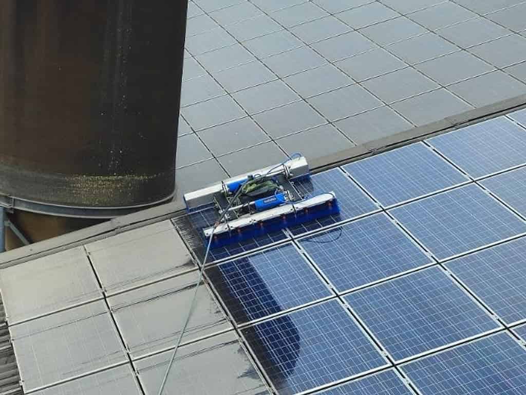 Waschroboter auf der Photovoltaikanlage eines Stalldachs neben einem Futtersilo, links noch grau verschmutzte Module, rechts schon gereinigte