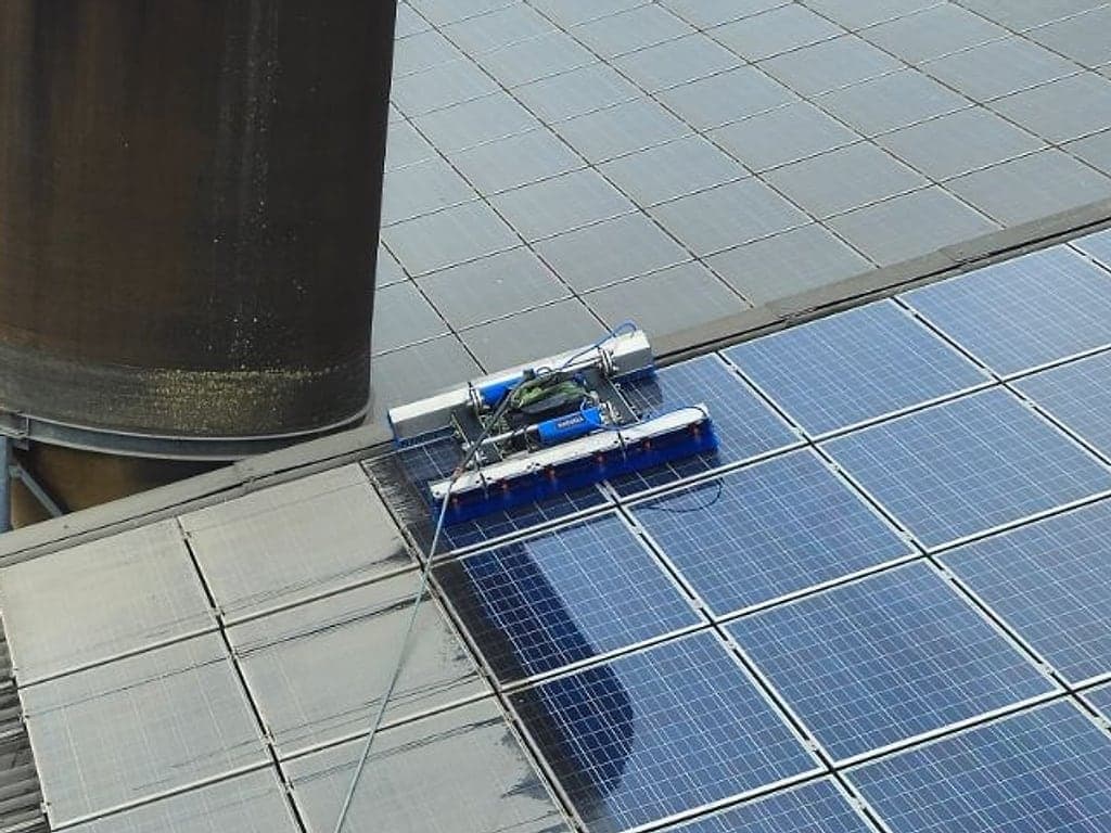 Waschroboter auf der Photovoltaikanlage eines Stalldachs neben einem Futtersilo, links noch grau verschmutzte Module, rechts schon gereinigte