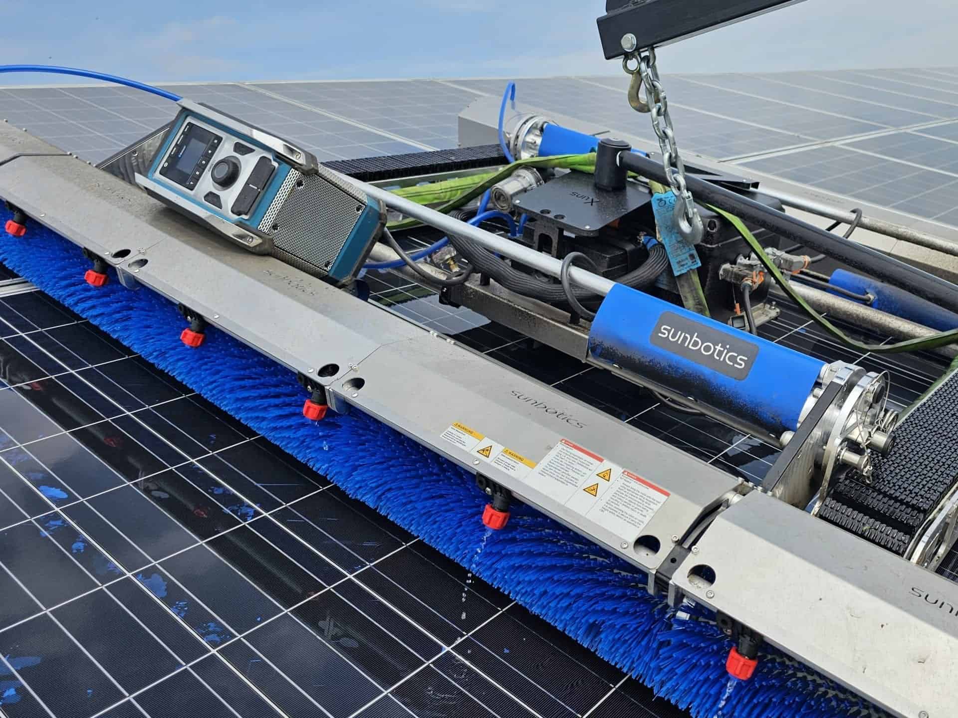 Waschroboter mit blauer Bürstenwalze auf nassen Photovoltaikmodulen